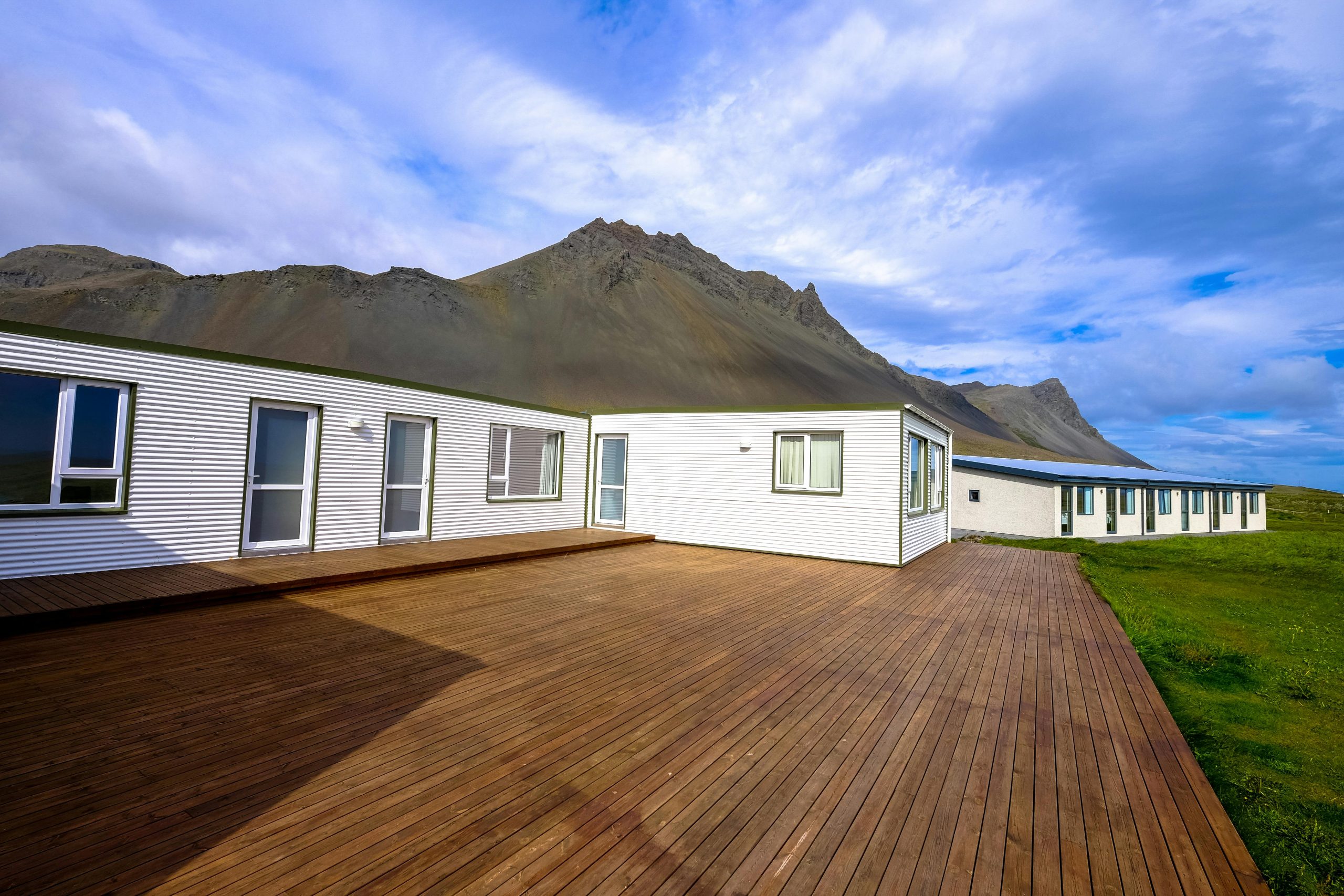 wooden deck extending from a white bungalow, with a mountain in the background